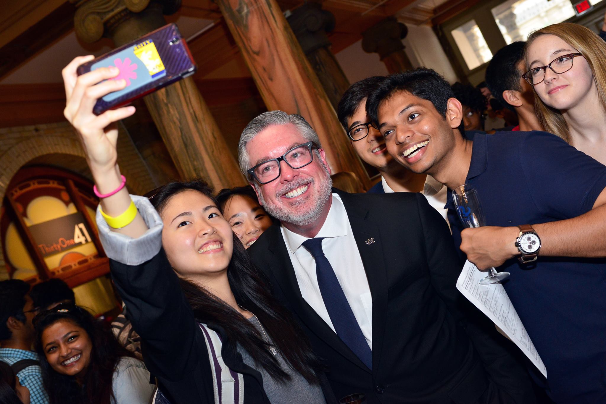 A different angle of President John Fry taking a group selfie with graduating seniors at the Senior Toast event which was held in the lobby of Main Building.