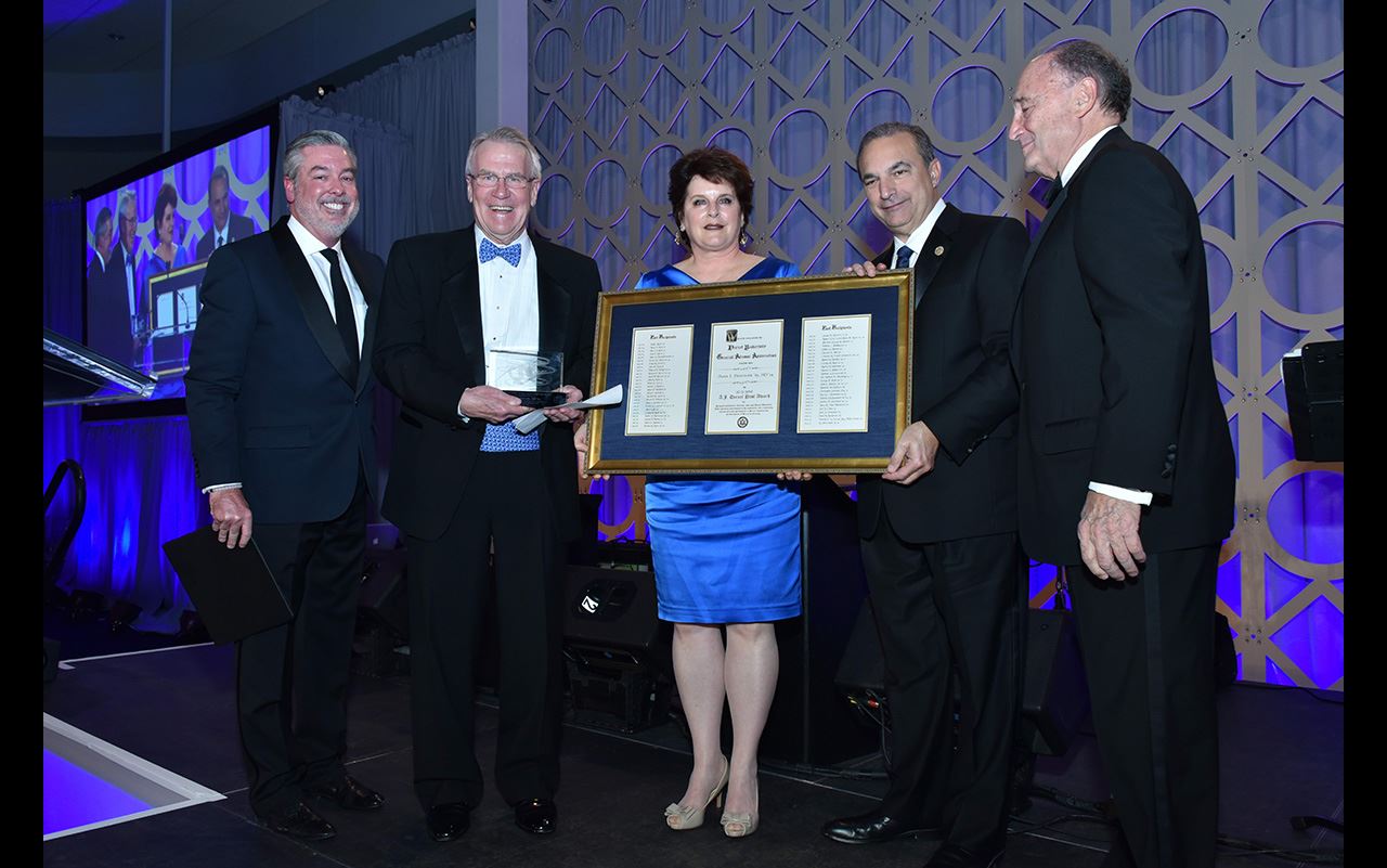 President John Fry posing for a photo with colleagues at the A.J. Drexel Society Gala. Two of his colleagues are holding a frame that has 3 documents.