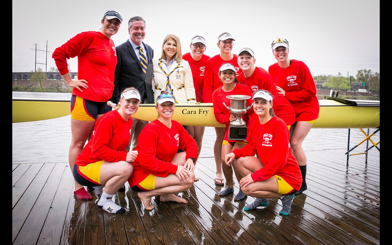 President John Fry standing with the Women’s Rowing team as they hold up their trophy from the 2017 Bergen Cup Regatta.