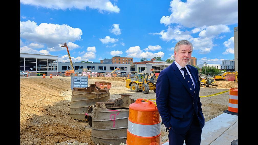 President John Fry standing in front of orange and white traffic drum at Powel Elementary / Science Leadership Academy Middle School and Drexel University Health Sciences Building site.