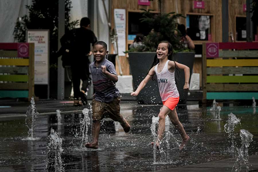 Two children running through water sprinklers at Dilman Park. 