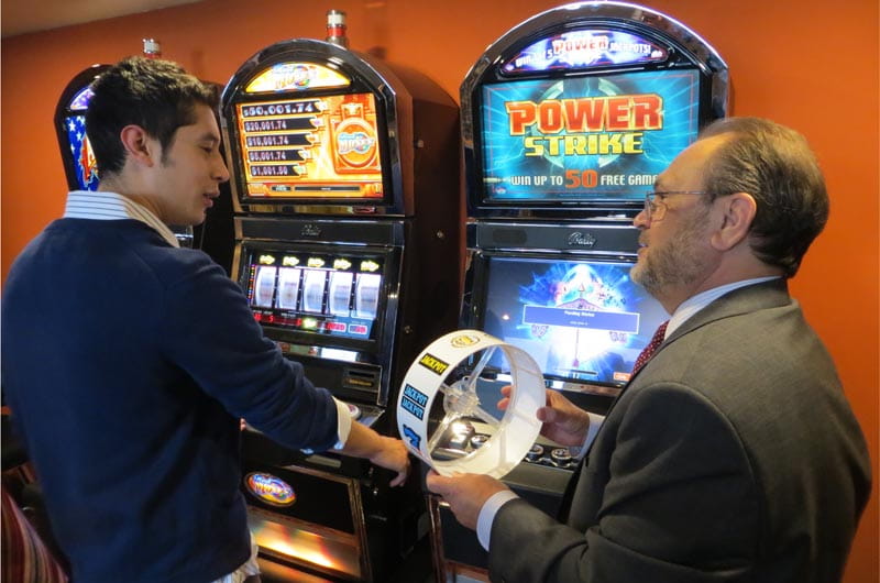 Instructor Bob Ambrose shows hospitality management major Andres Roos a reel strip from one of the slot machines in the Dennis Gomes Memorial Casino Training Lab.