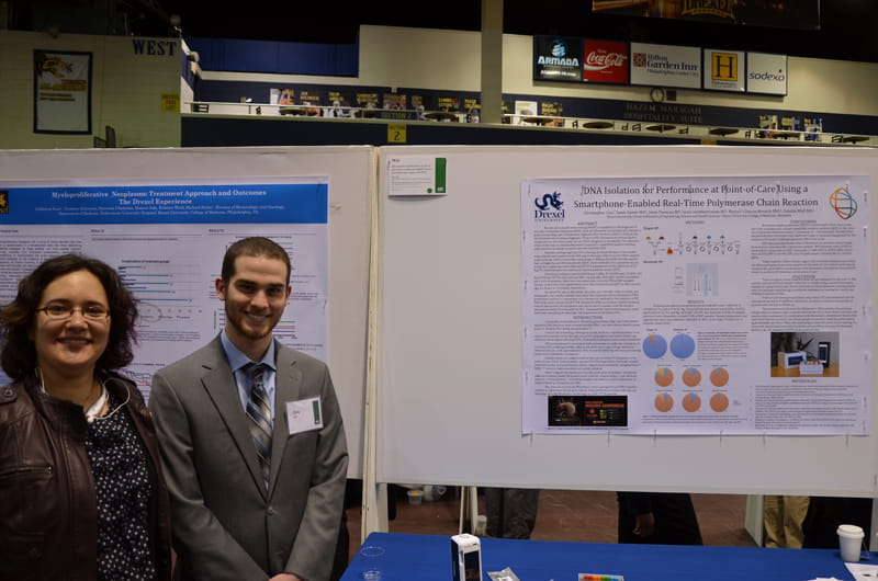 At right, Chris Cox, the student researcher, and Maria F. Chacon-Heszele, PhD, (left), an advisor, in front of a research poster on a kit designed to give real-time medical test results for detecting sexually-transmitted diseases.