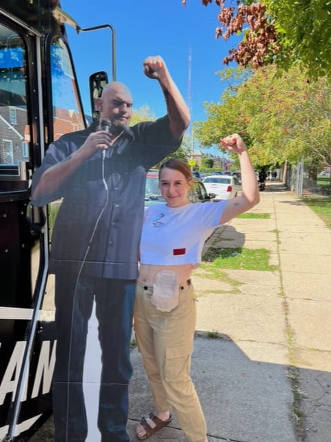 Claire Wessels with an ostomy bag, posing next to a cardboard cutout of Senator John Fetterman