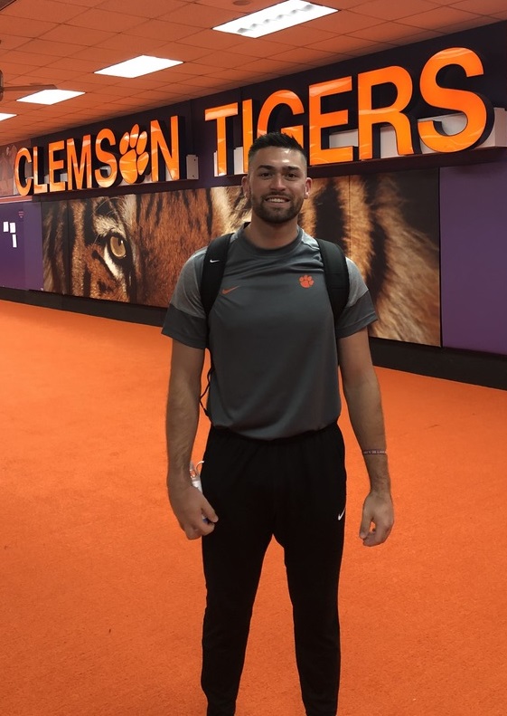 White male wearing a Clemson Tigers staff uniform standing in front of a larger tiger graphic.