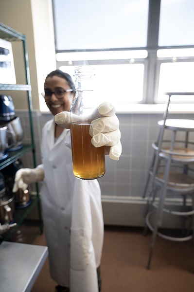 Drexel Food Lab student holding a beaker filled with an amber liquid as she works on a beverage made from avocado seeds.