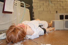 Manakin with moulage on face on floor near fallen bricks.