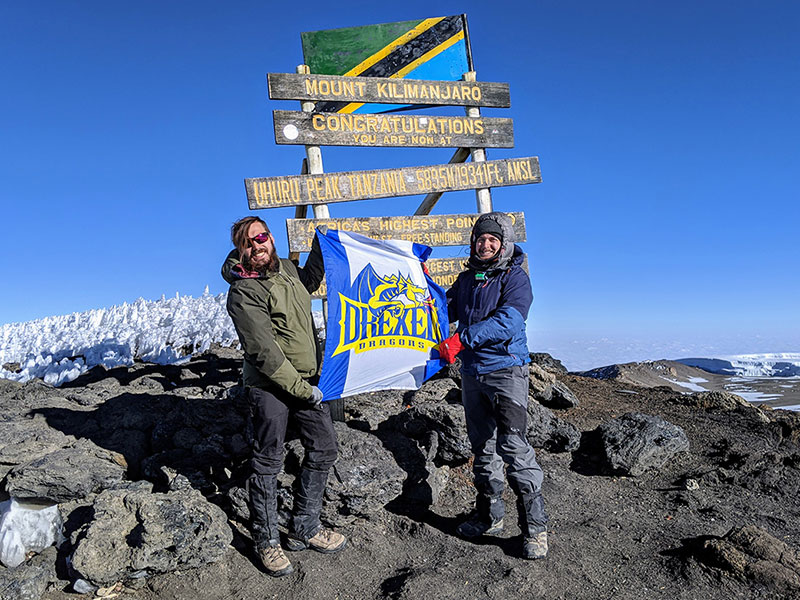 Two students hold a Drexel flag at the top of Mount Kilimanjaro.