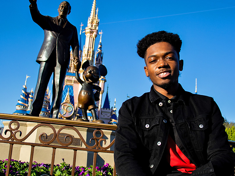 Young man in front of statue of Walt Disney and Mickey Mouse