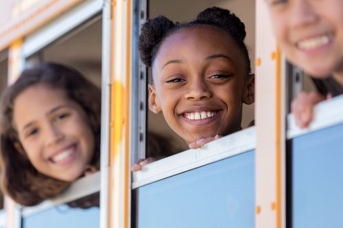 Children smiling and looking out open school bus windows