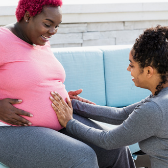 Pregnant woman with doula touching baby bump.
