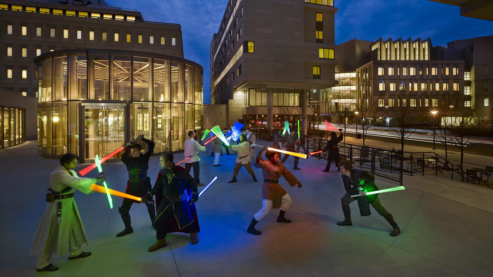 Members of the Dragon Jedi club outside on campus. They are wearing long robes and other Star Wars inspired attire while reenacting battles using fake lightsabers.