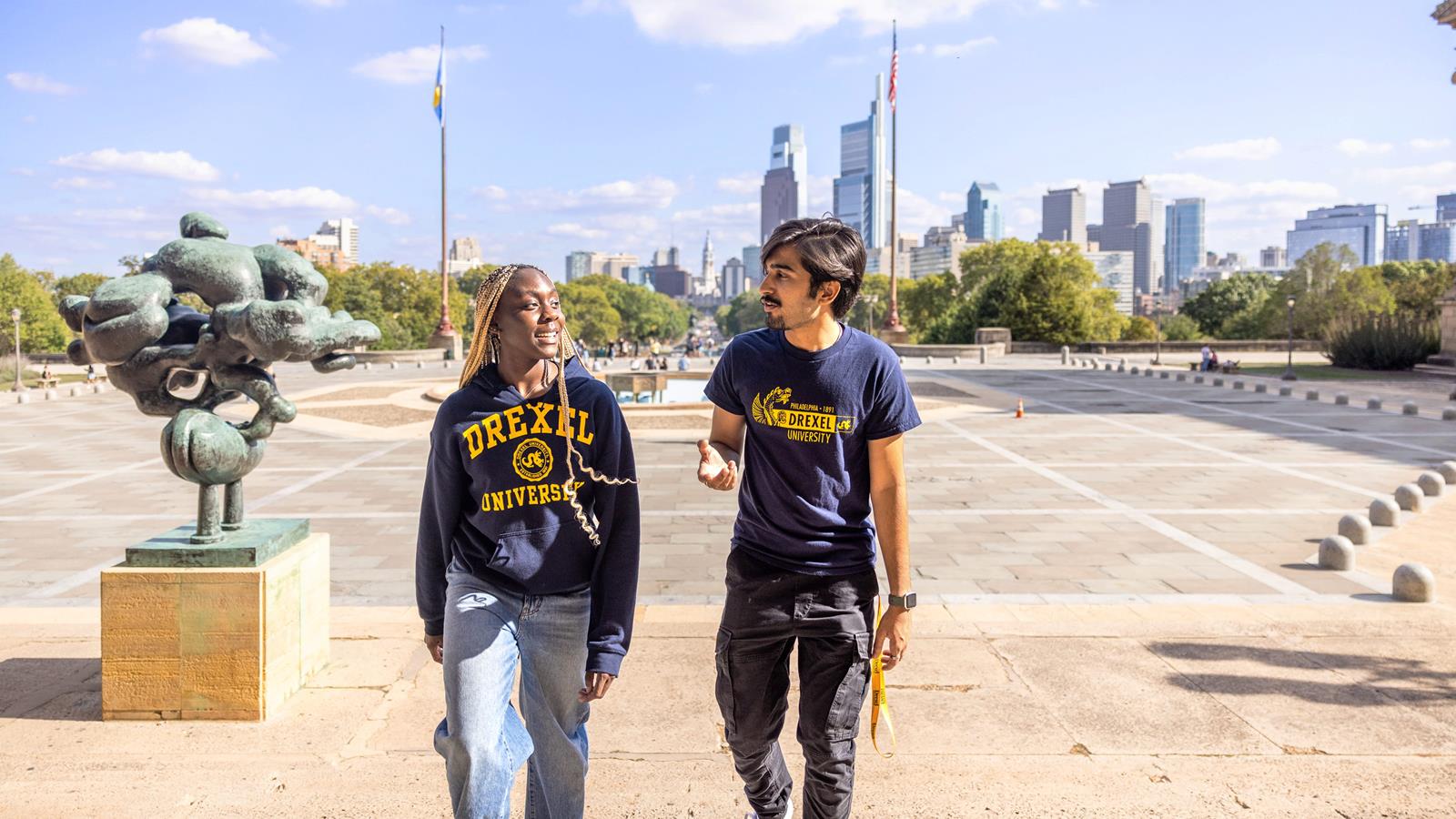 A female student and male student in Drexel attire talking and walking up the steps of the Philadelphia Art Museum.