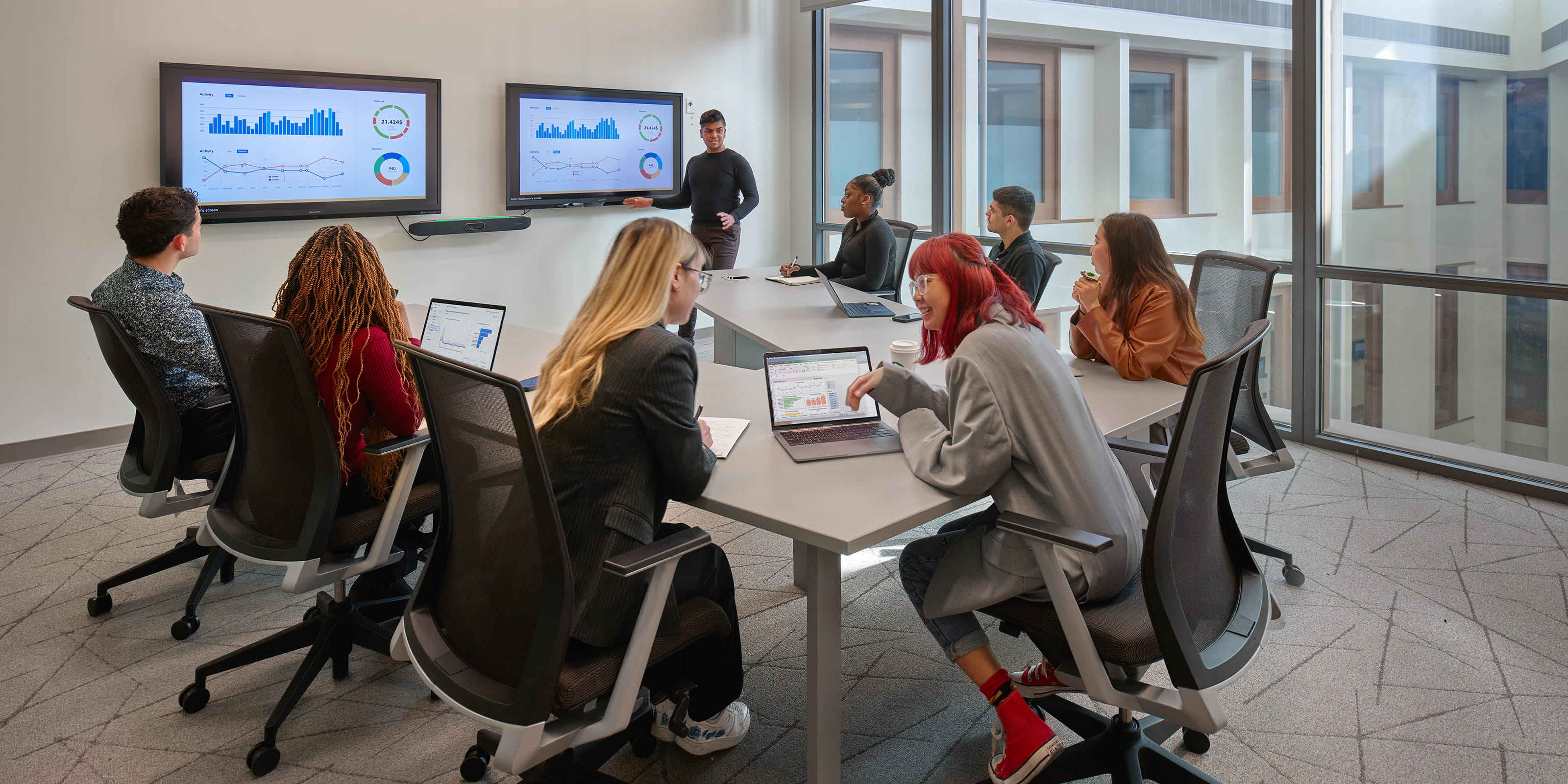 A student giving a financial presentation to a group of fellow students in a conference room
