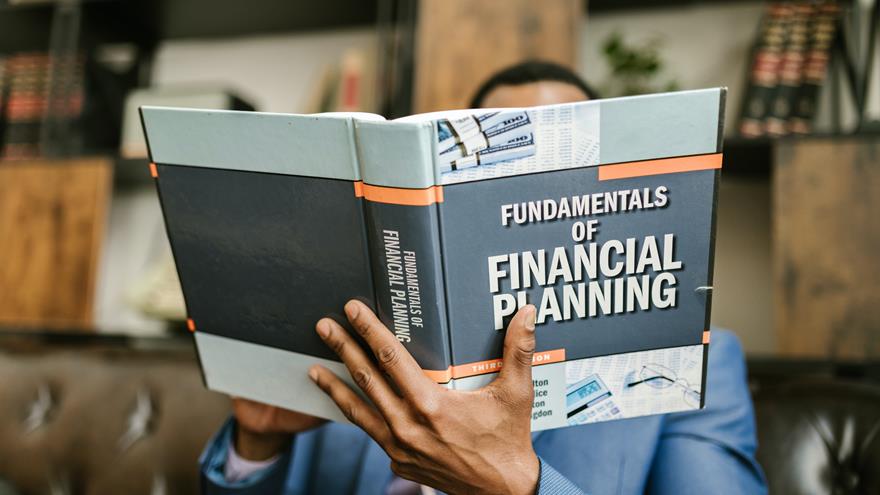 Person holding up book titled "Fundamentals of Financial Planning"