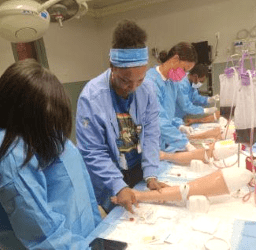 a group of people in blue medical worker smocks practice blood draws on fake arms