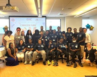Image of a large, diverse group of people smiling in front of a projection screen in a classroom
