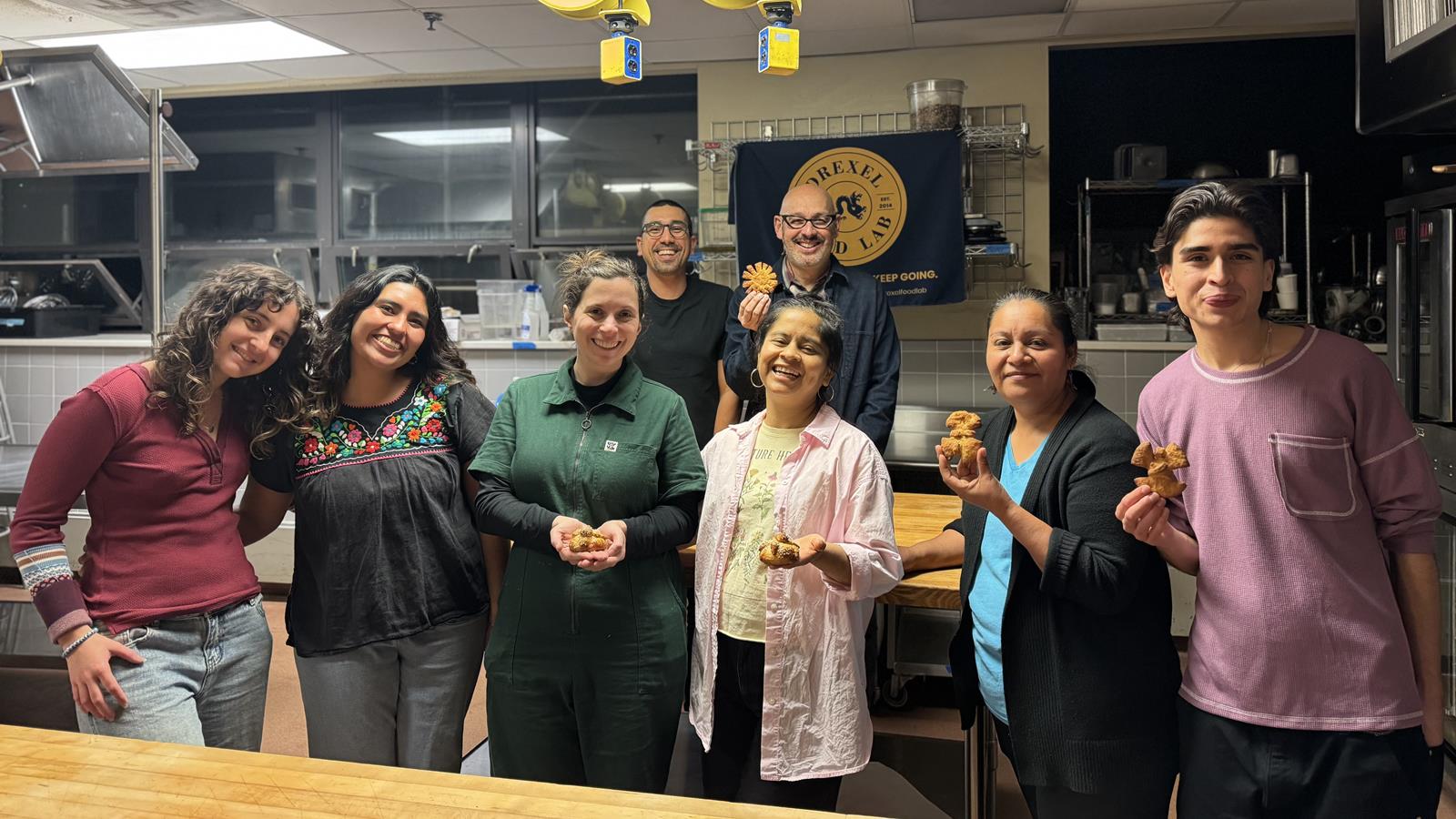 a group of 8 smiling people stands together in a kitchen