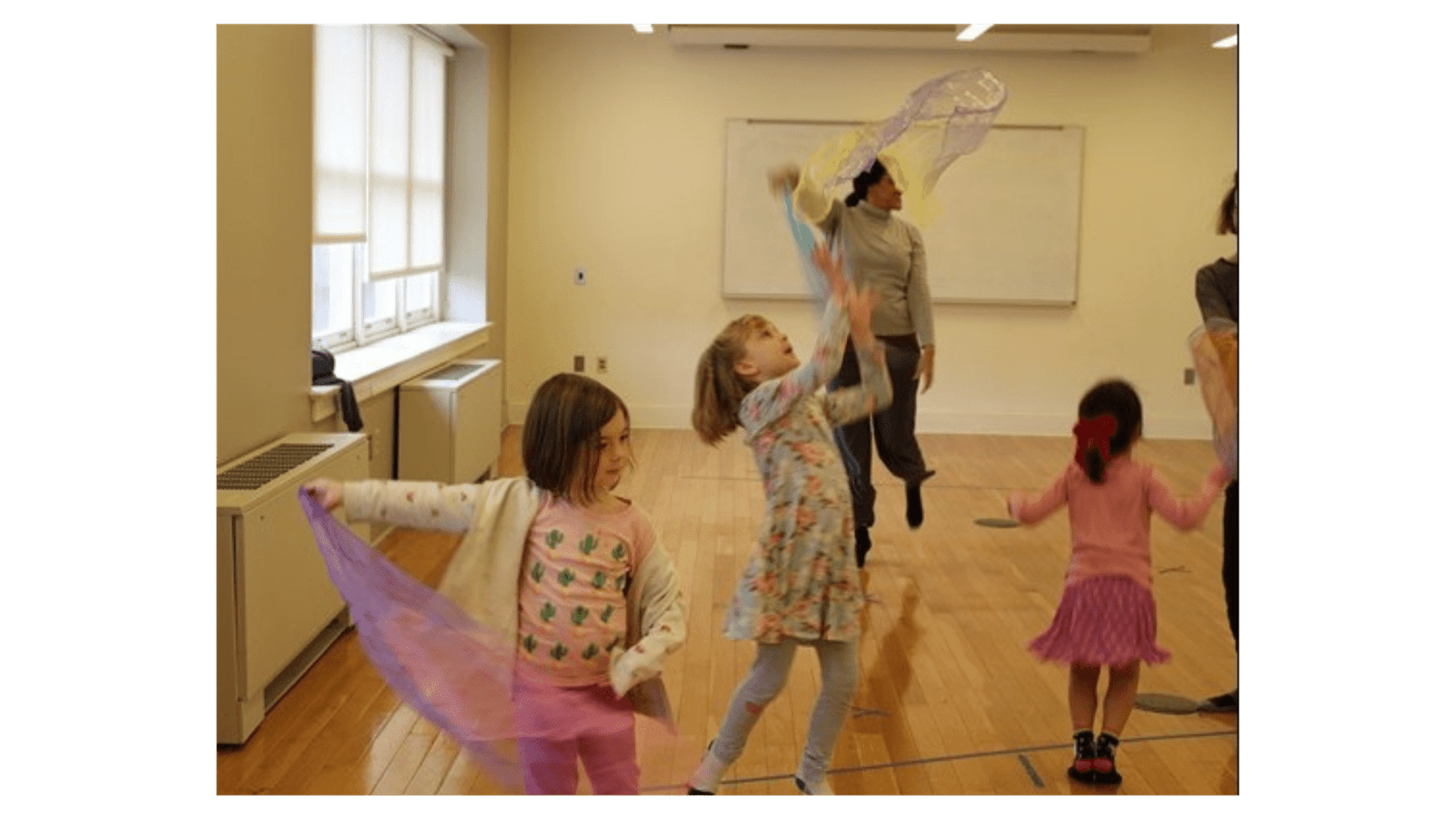 image shows three children dancing around a room with colorful outfits and colorful scarves