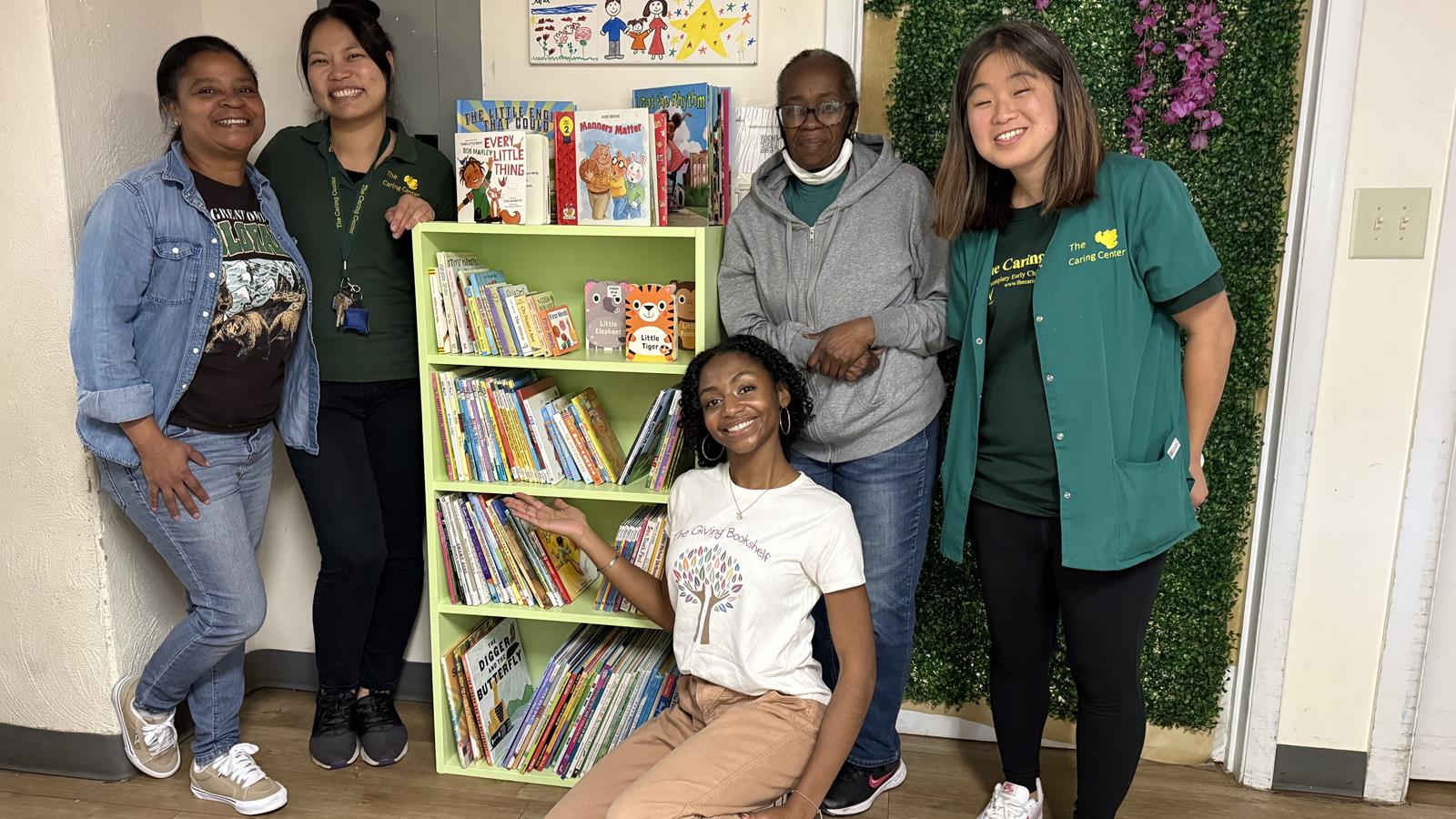 A group of 5 people pose around a bookshelf smiling at the camera. 