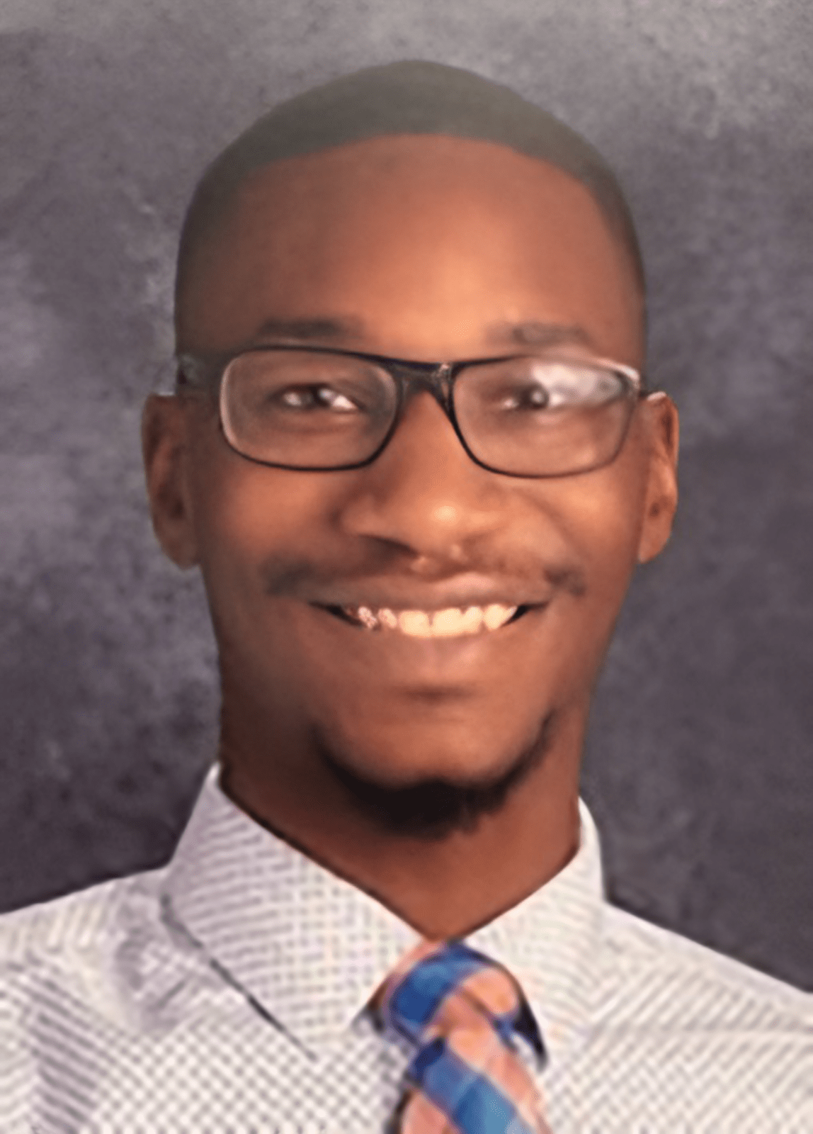 smiling person with glasses, white shirt, and tie and gray background