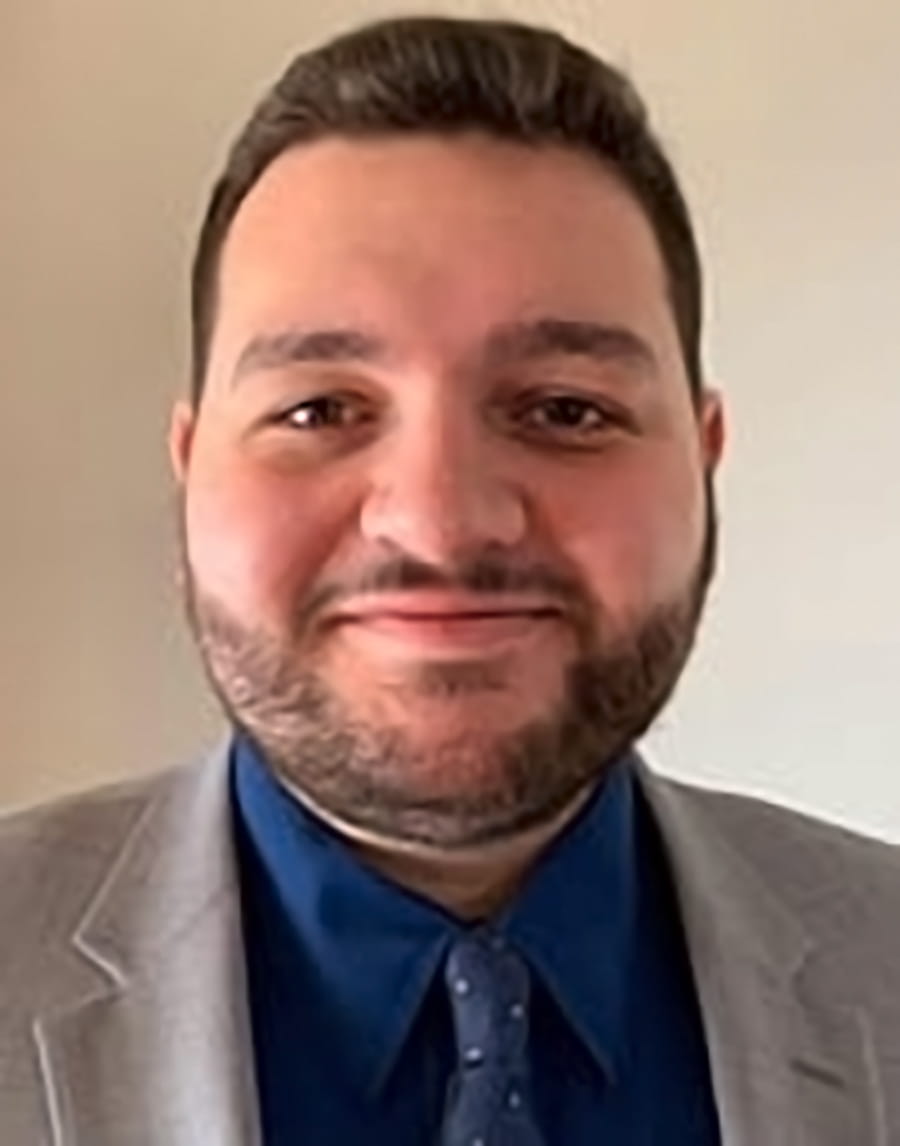 Smiling person wearing gray blazer and blue shirt and tie