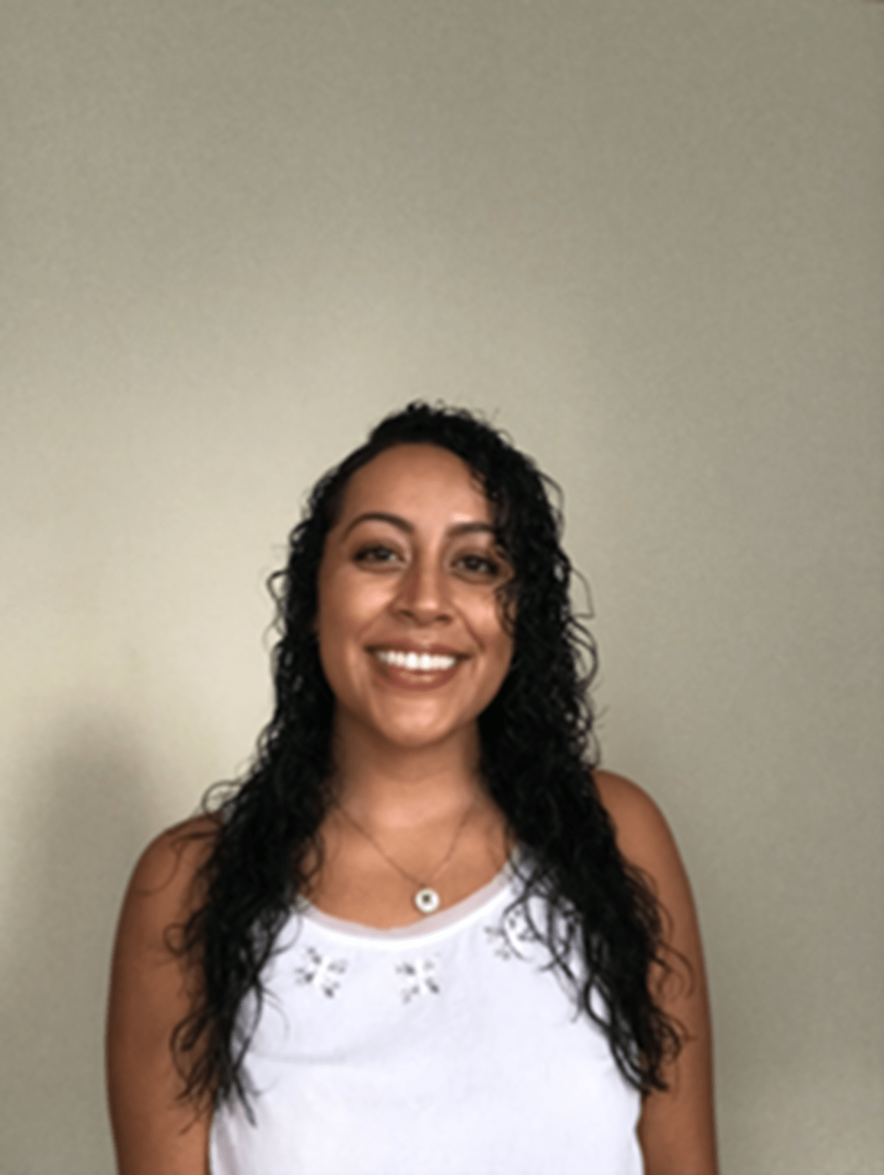 Smiling person with long dark hair and wearing white shirt 