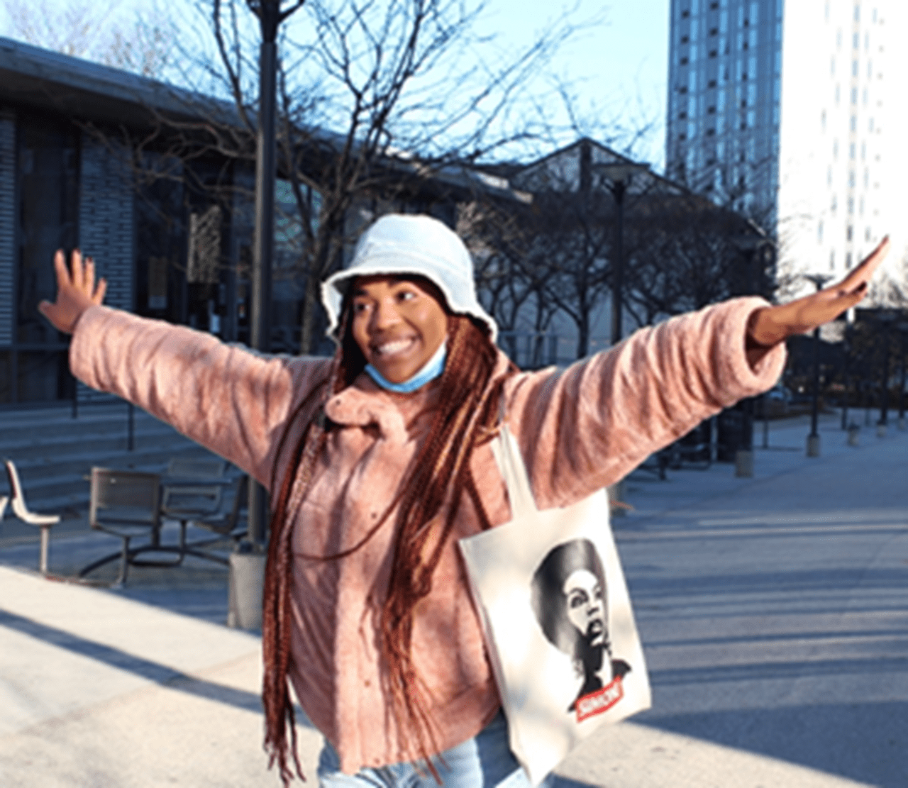Person smiling with arms outstretched wearing white hat and pink jacket