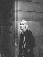 black and white photo of person standing against a wall smiling wearing a jacket