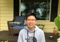 Person smiling in front of a porch and window wearing a gray sweatshirt and glasses
