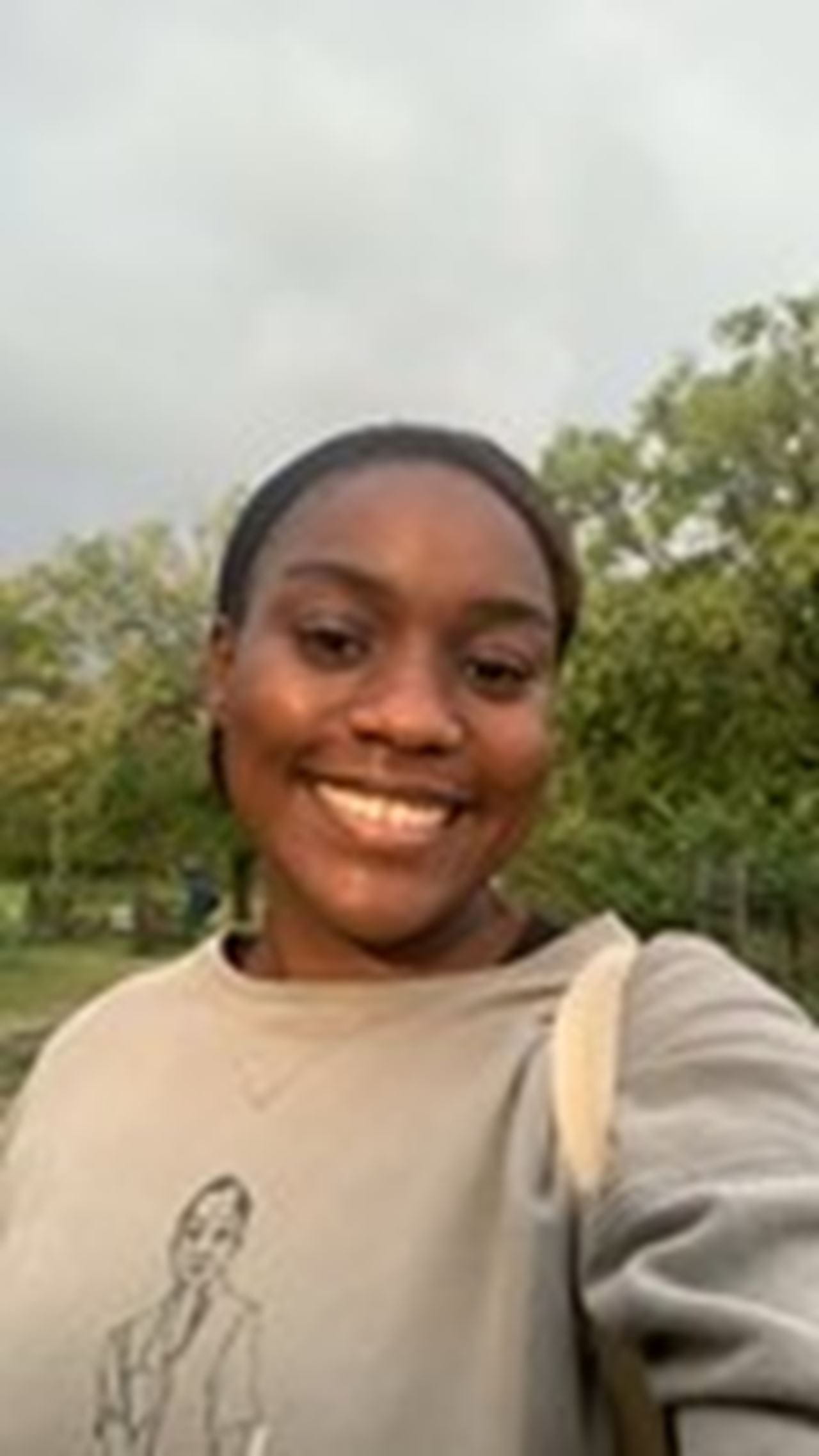 Person smiling outside wearing a gray sweatshirt