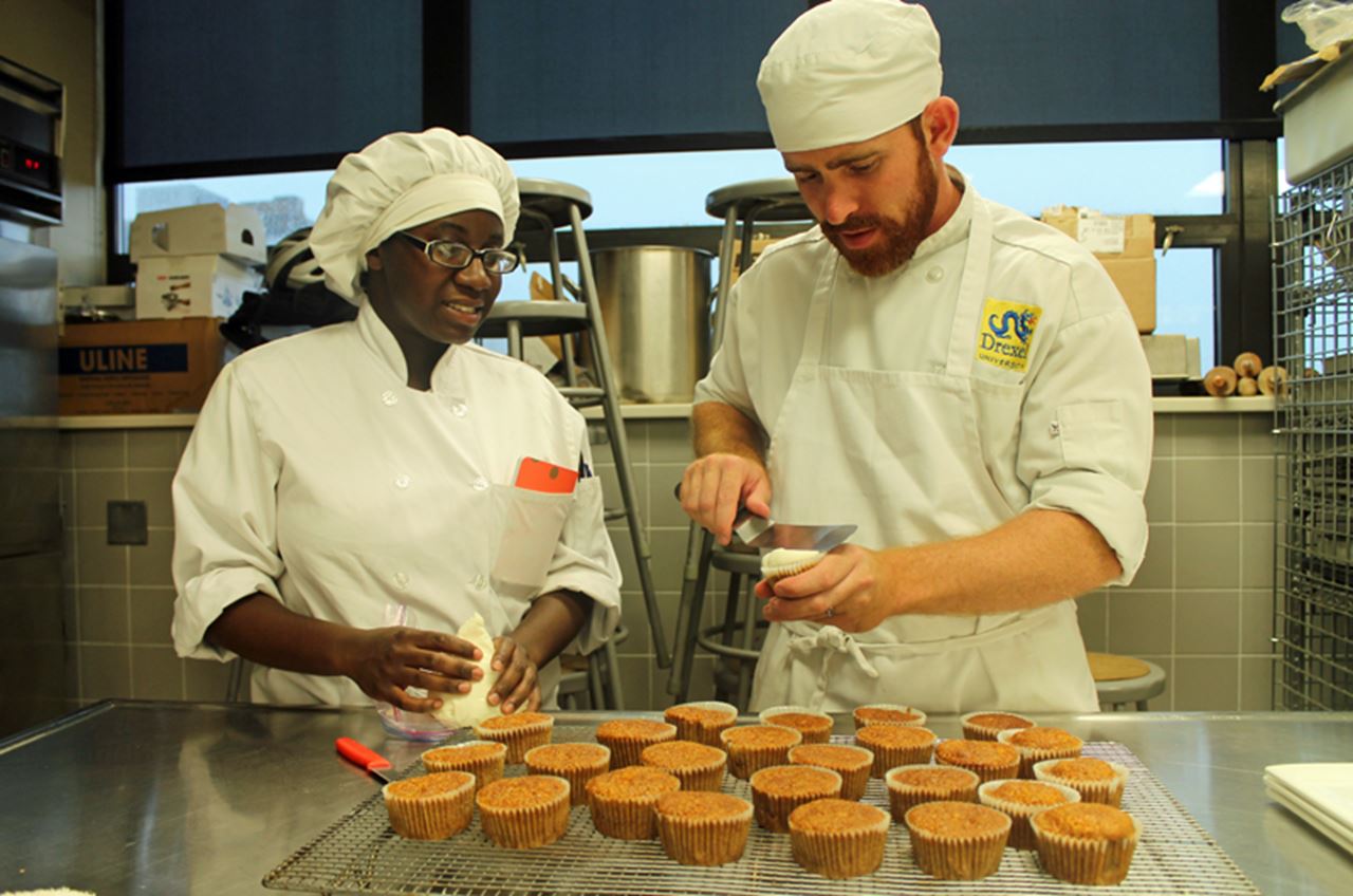 Drexel hospitality management student Matt Sandrowski shows a classmate how to make his mother’s carrot cake recipe