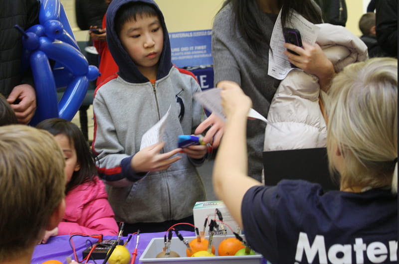 Young boy learns about making batteries from fruit from Drexel materials science students.
