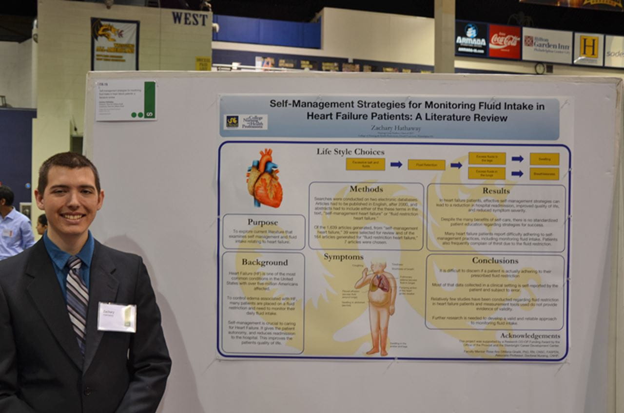 Zachary Hathaway stands in front of his poster on research into monitoring food and fluid intake for those who have suffered heart failure.