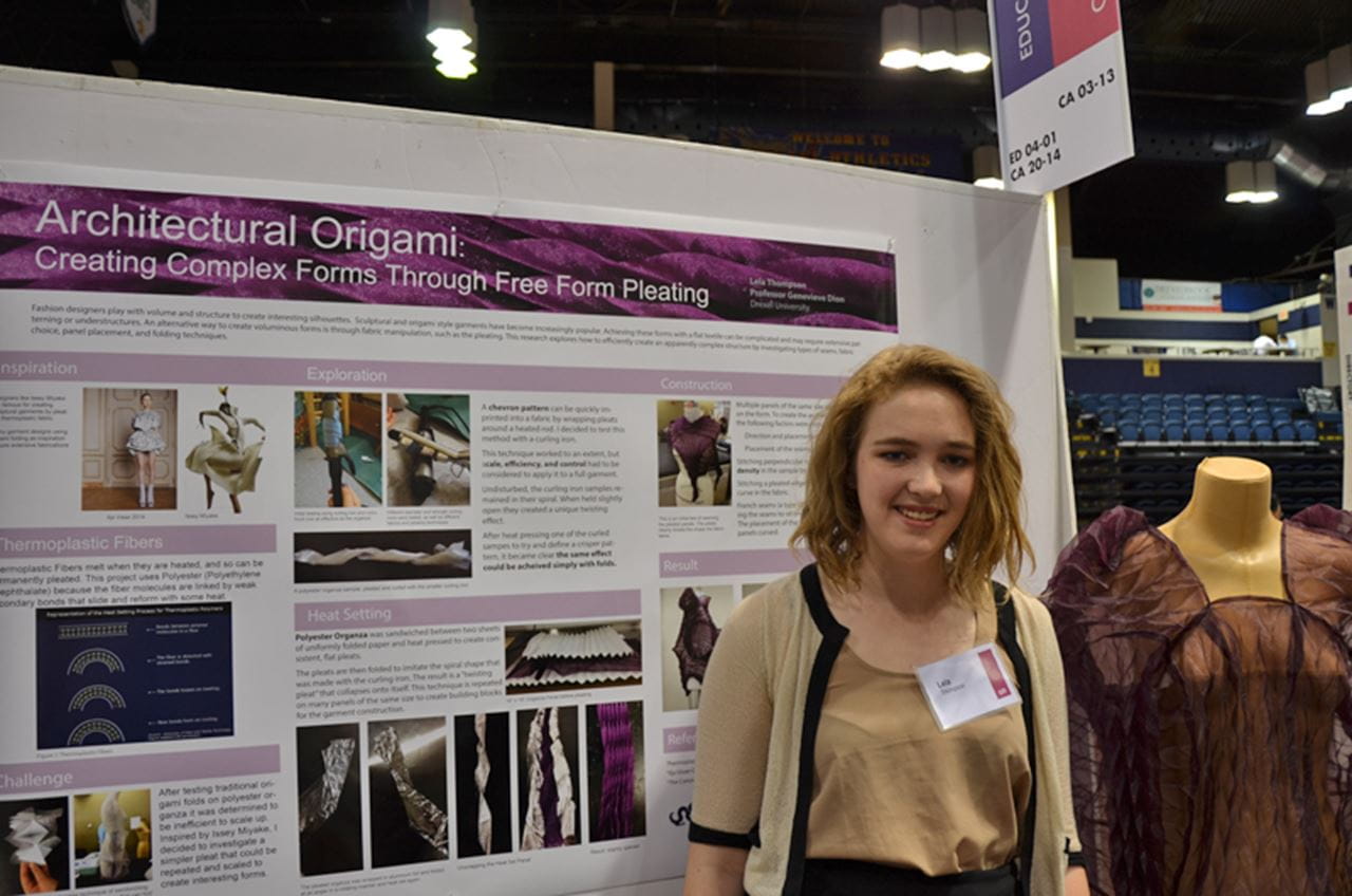 Lela Thompson with her research poster on experiments with design to create origami-style garments, like the dress at her left.