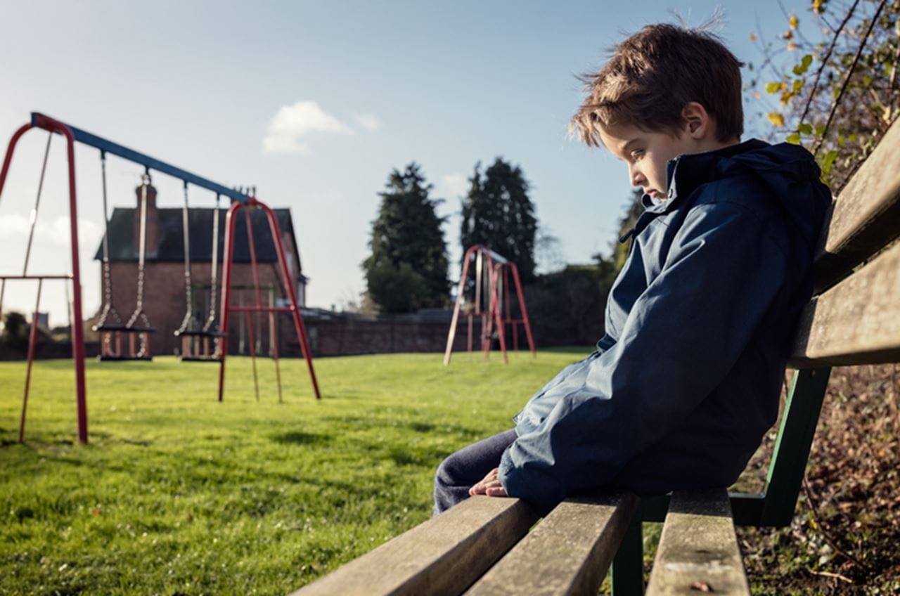 A child sitting on a park bench looking sad