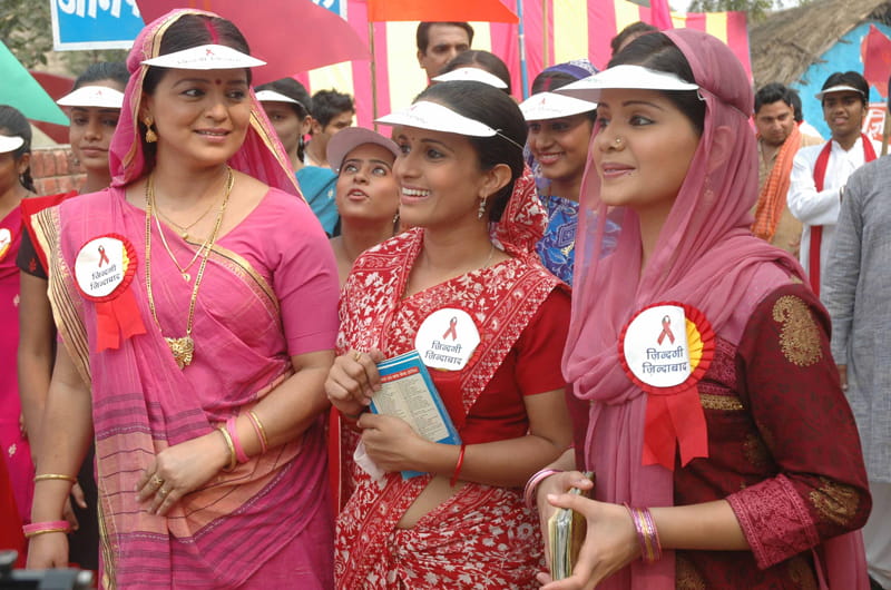 A group of women wearing visors and buttons with red ribbons for HIV awareness.