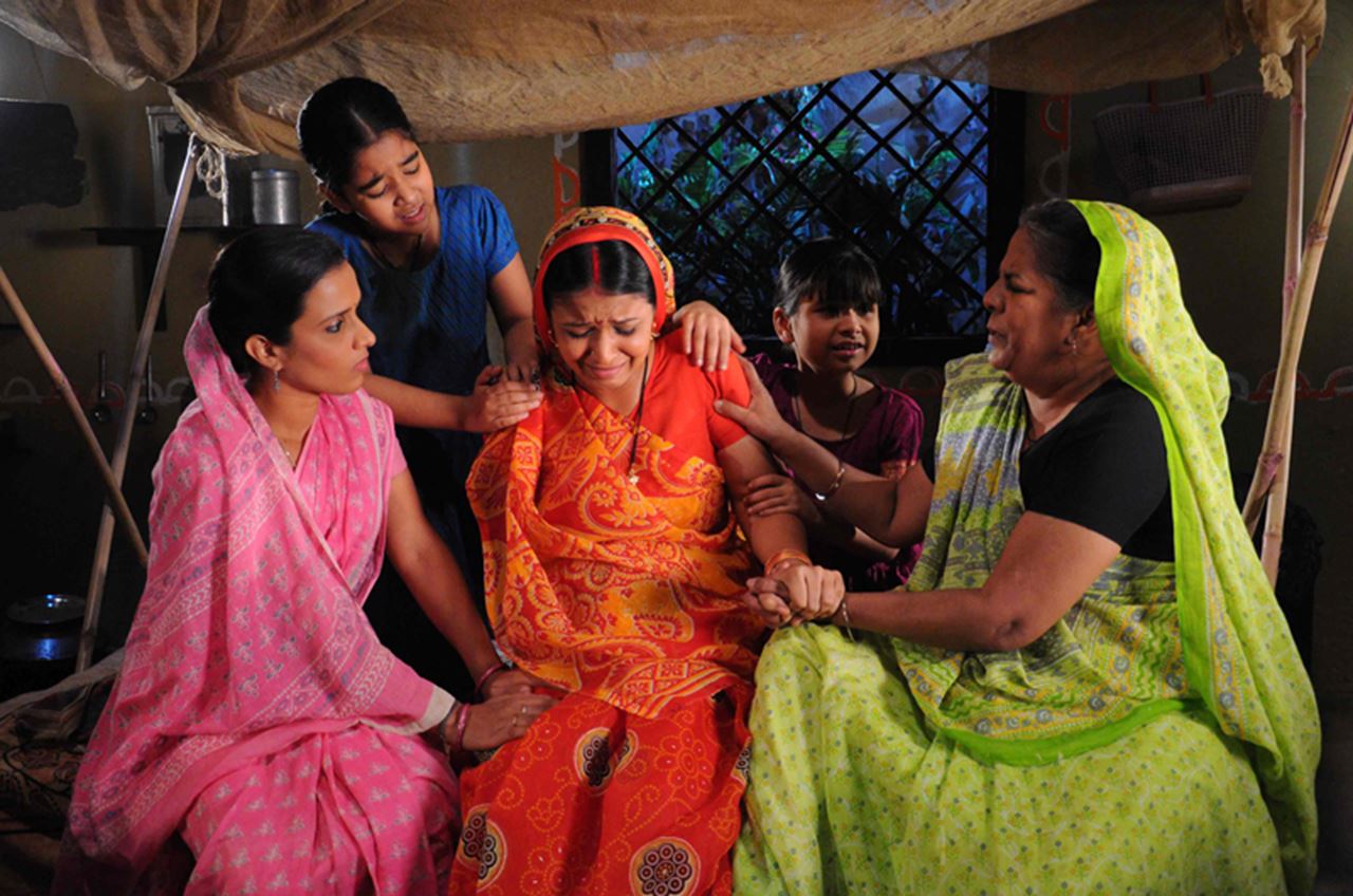 A group of women in sarees comforting each other.