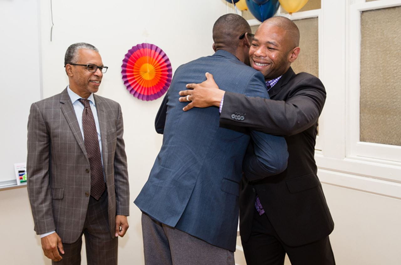 Ted Corbin hugging a graduate of the program while John Rich looks on.