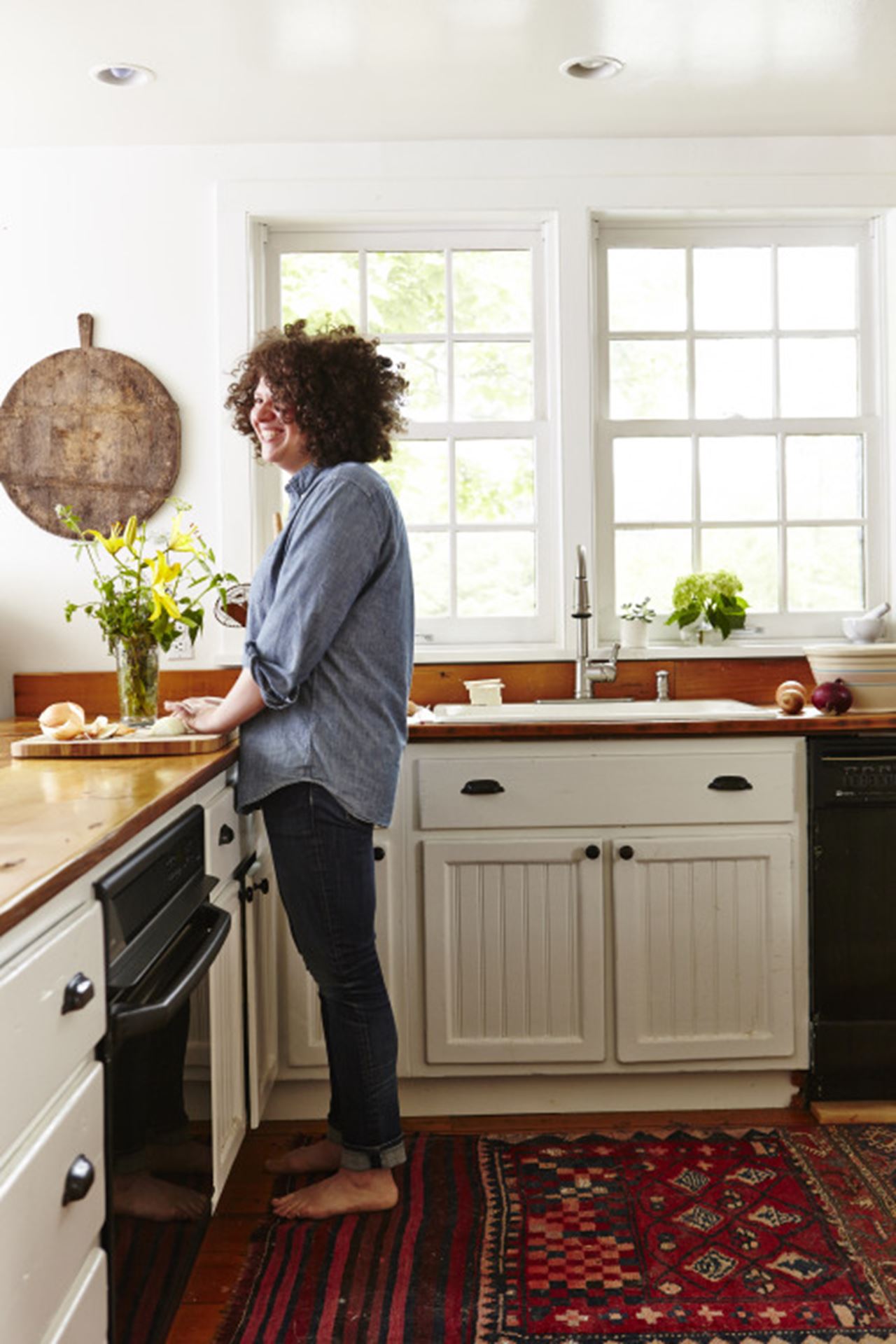 Julia Turshen standing in a kitchen in front of a cutting board where she is slicing onions.