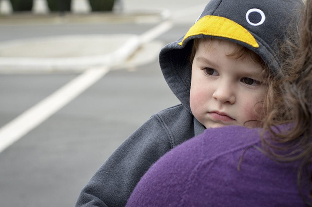 A child being held by a mother and looking over her shoulder.