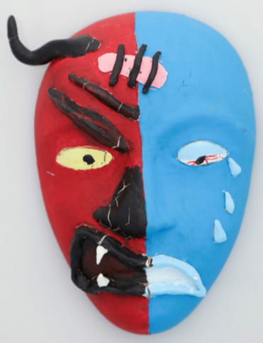 A mask that is split down the middle, with the left side seeming to depict a red, devil-like face and the right painted blue and showing a sad, human-like face with a band-aid between the two.