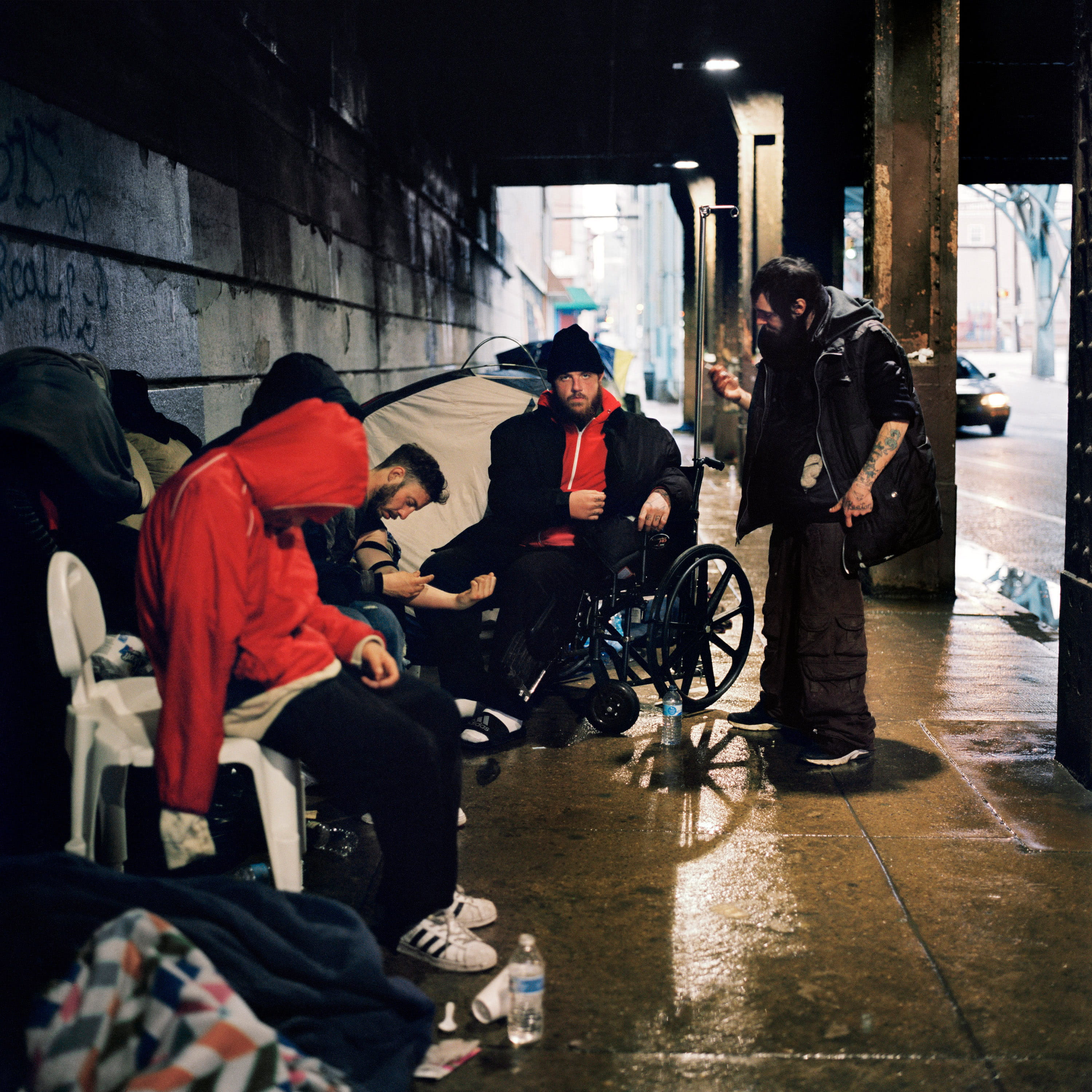 Beneath the Kensington Avenue underpass, 2018. Chris (right) prepares to inject John (center) in the neck beneath the Kensington Avenue underpass. Heroin users often rely on one another to inject their drugs for them when the veins in their arms, legs, hands or feet are no longer receptive. 