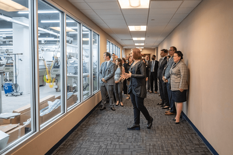 Director Geneviève Dion leads tour guests, including Neil Weaver (far left), Secretary of the Department of Community and Economic Development from the office of Governor Tom Wolf, as they view the manufacturing space for the first time before entering. The machinery/technology in the space was funded in part by a $1.5 million grant from the Commonwealth of Pennsylvania.