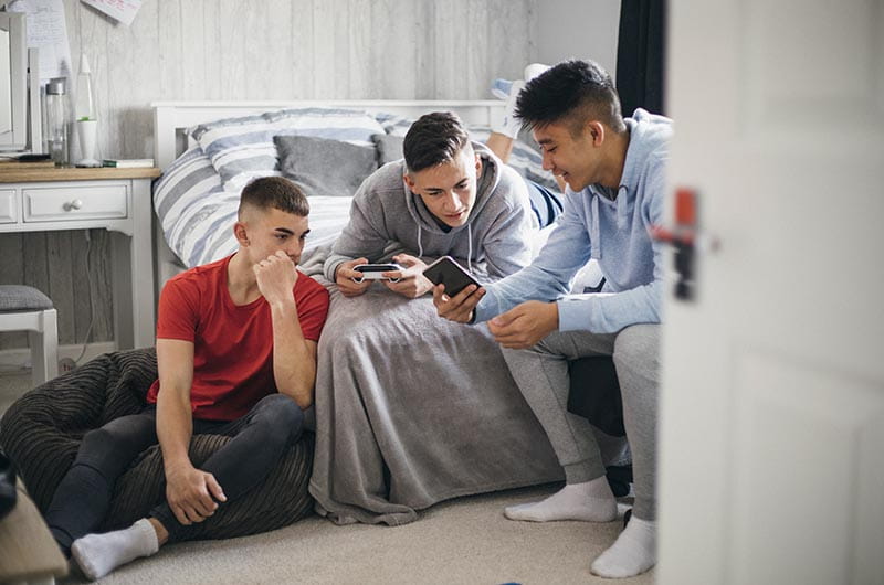 Three teenage boys playing video games in a bedroom