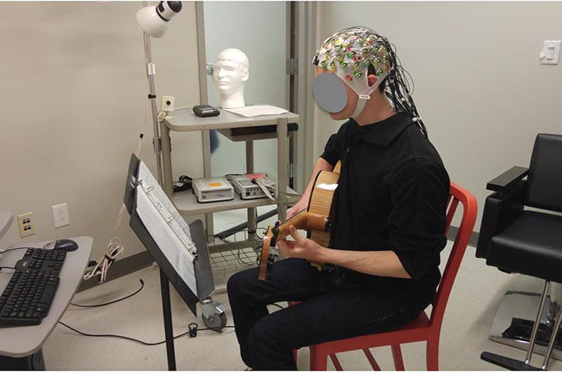 Unidentified male playing guitar while his brain activity is recorded. 