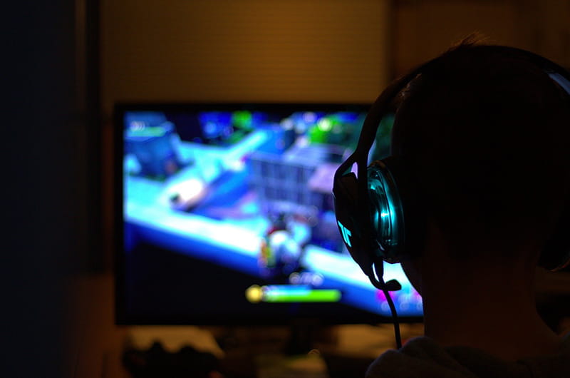 Silhouette of a person with headphones on in front a monitor playing a video game. 