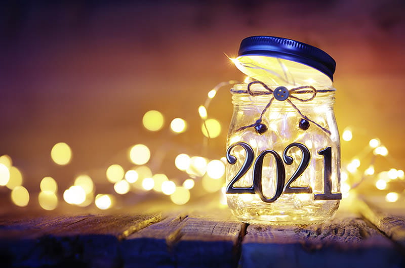 A mason jar labeled 2021 with fairy lights around it on the table.