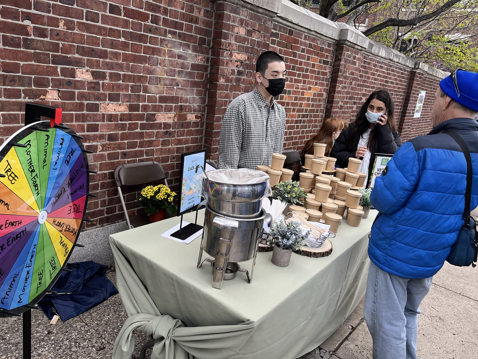 EarthFest participants stand on Lancaster Walk at a table with a metal pot and cardboard takeout containers.