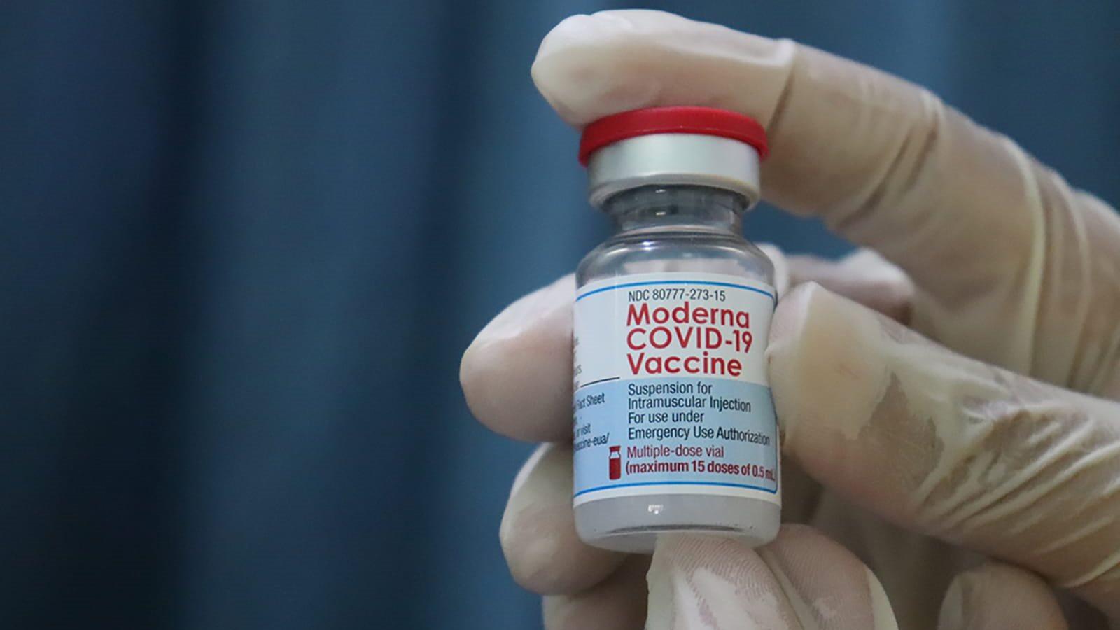 Gloved hand holding COVID-19 vaccine vial